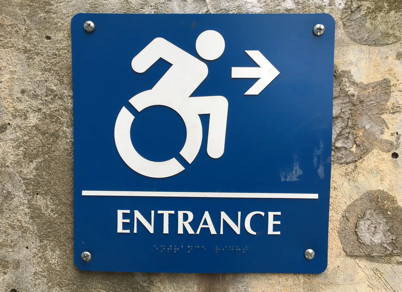 Blue accessible entrance sign with the dynamic accessibility symbol